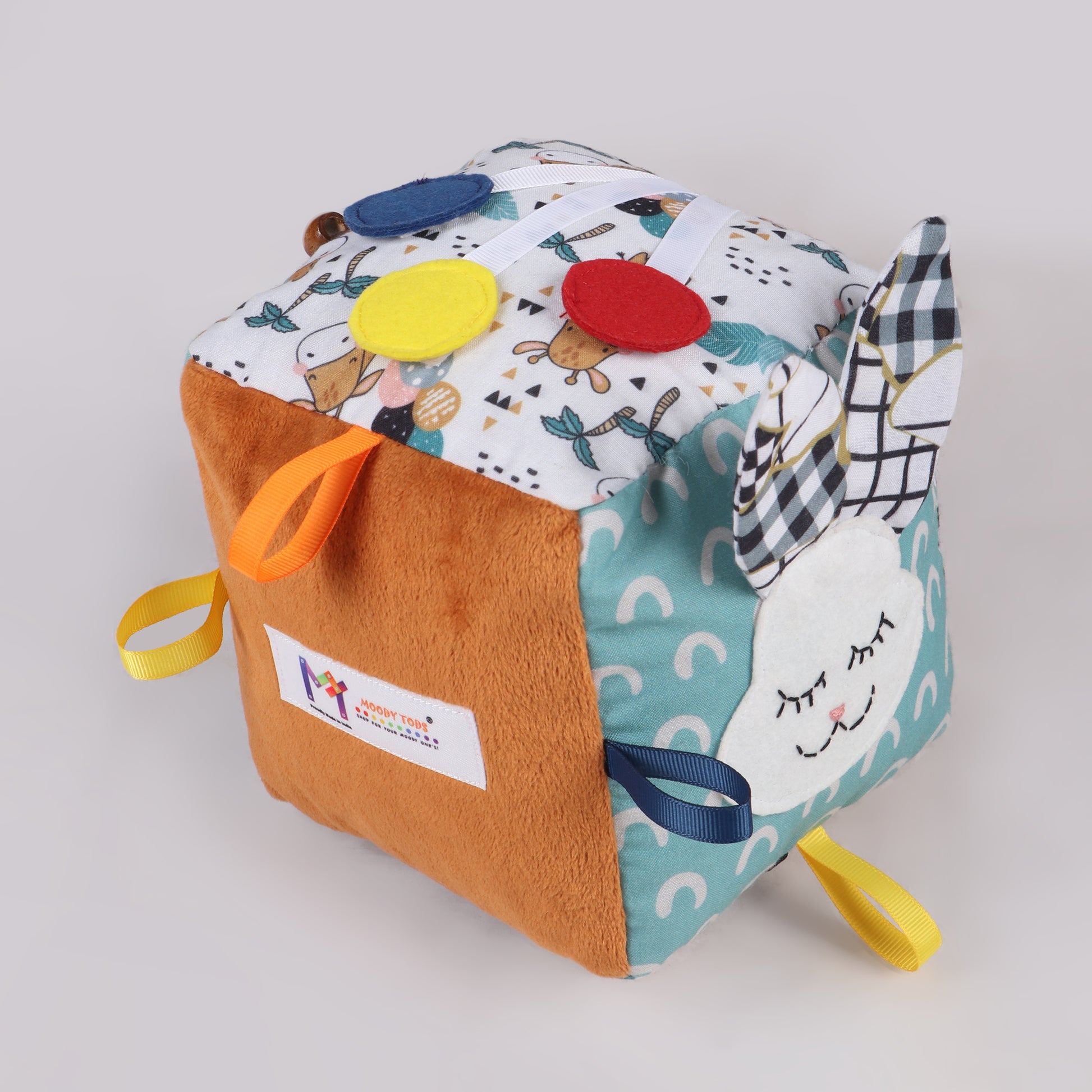 Side view of soft fabric activity cube with interactive elements like ribbons, textures, and buttons for early childhood development