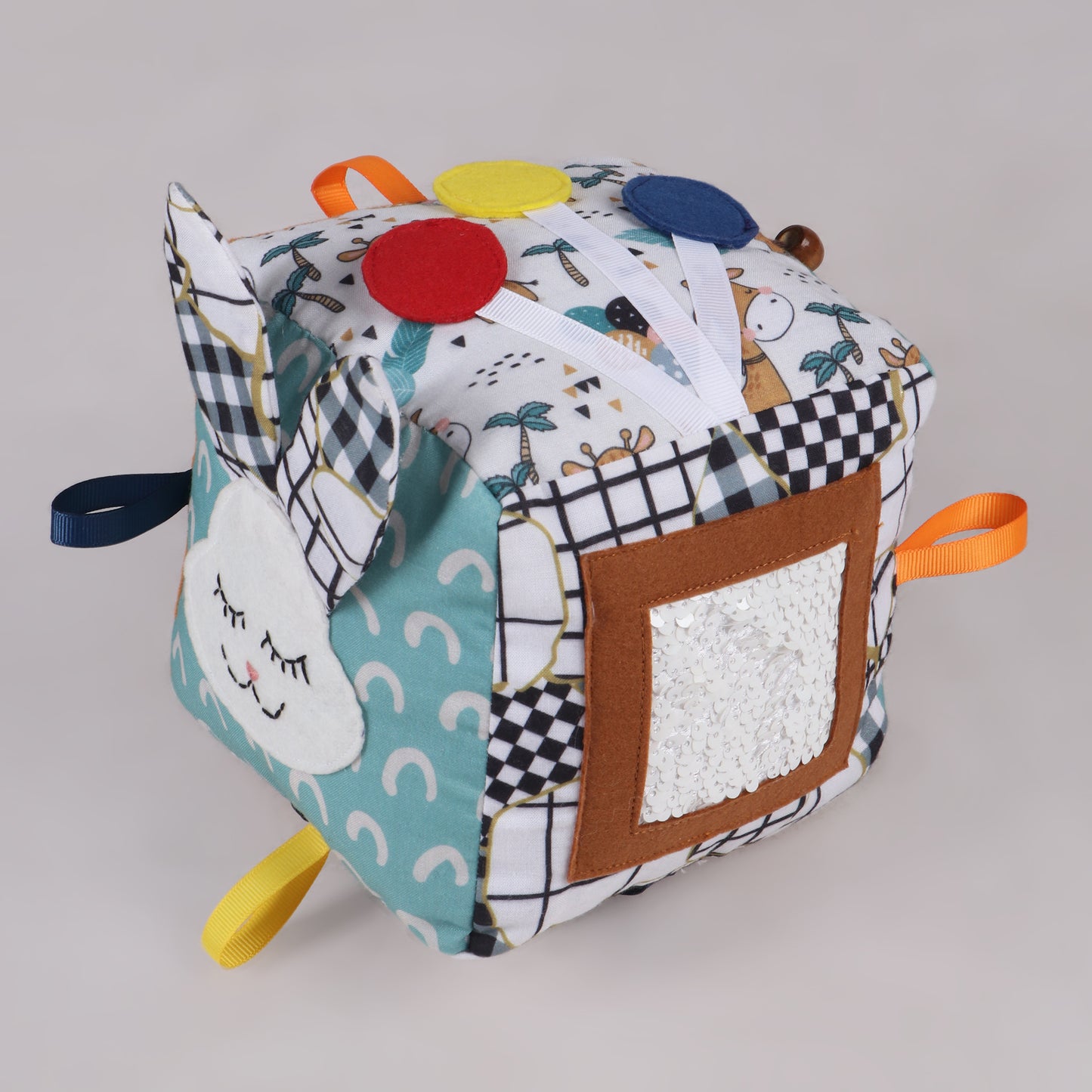 Side view of soft fabric activity cube showing sequin activity and bunny with its ears popping out of cube with interactive elements like ribbons, textures, and buttons for early childhood development