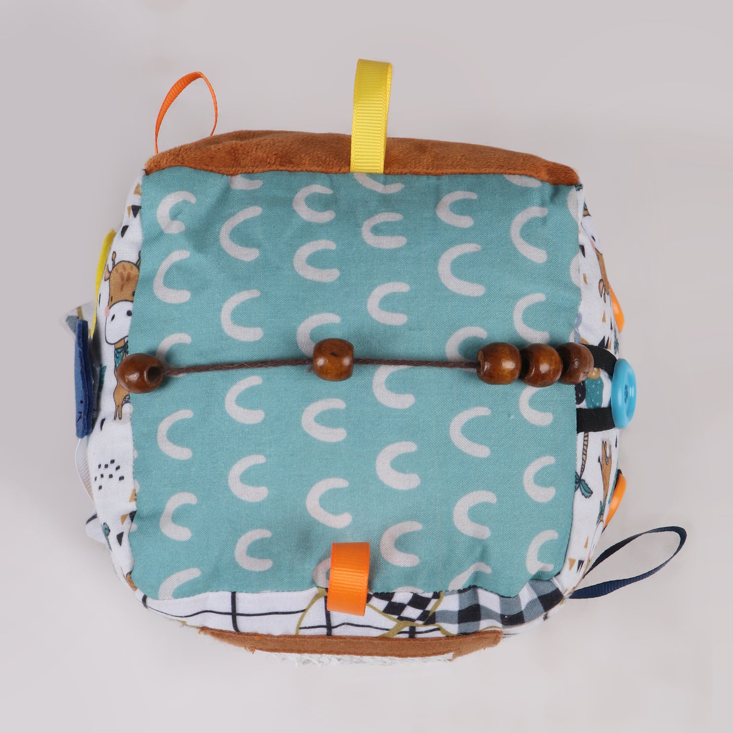 Top view of bead activity of soft fabric activity cube with interactive elements like ribbons, textures, and buttons for early childhood development