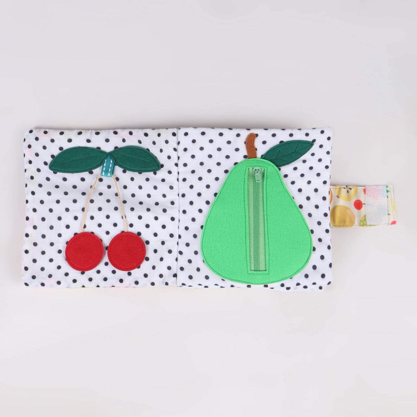 Interactive fabric fruit book featuring a cherry to pluck and a zipper revealing the inside of a pear, designed for sensory learning and fine motor skill development