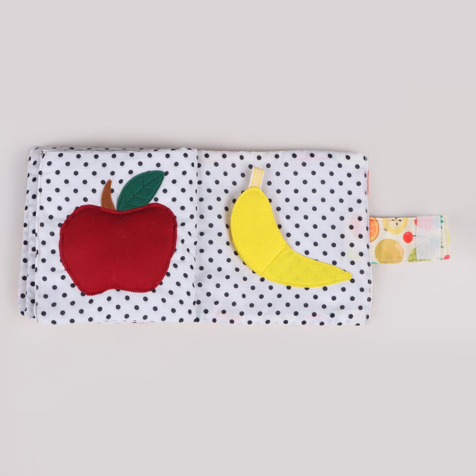 Interactive fabric fruit book featuring a squeaky apple that makes a sound when pressed and a banana with Velcro, allowing a peeling action for sensory and motor skill development