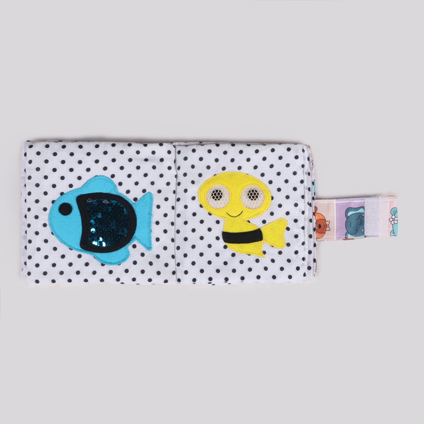 Sensory fabric book featuring a fish with sequins on its body to mimic skin texture and bees with movable eyes enclosed in a net for a tactile exploration experience, promoting sensory development and fine motor skills