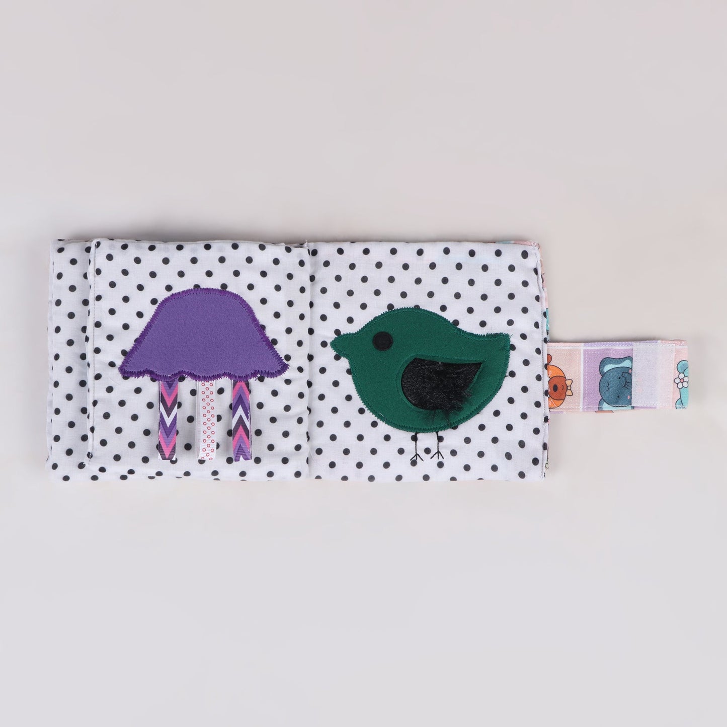 Sensory fabric book featuring a bird with soft-textured wings for a gentle tactile experience and a cloud-shaped element with three pullable ribbons, encouraging fine motor skills and sensory exploration