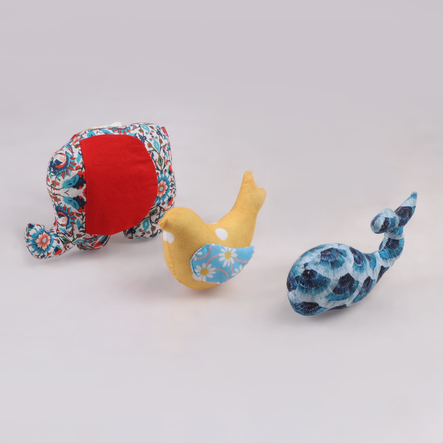 Elephant, Bird and Shark-shaped sensory taggie toy in standing position with big red, blue and yellow colored fabric for tactile exploration and comfort