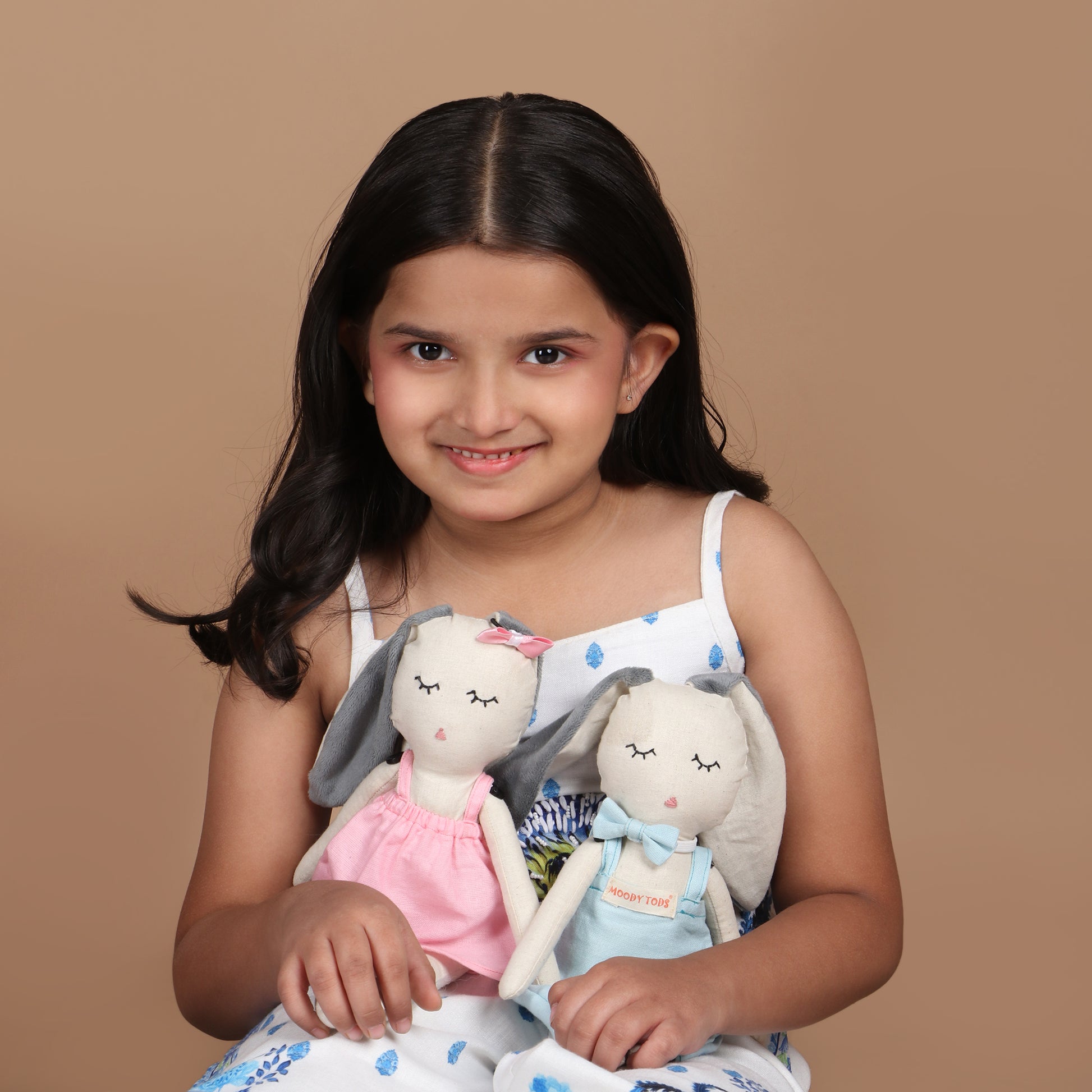 Little girl holding Pair of an adorable 12 inch plush bunny toys with blue and pink pastel colored outfit, demonstrating its child-friendly size and comfort