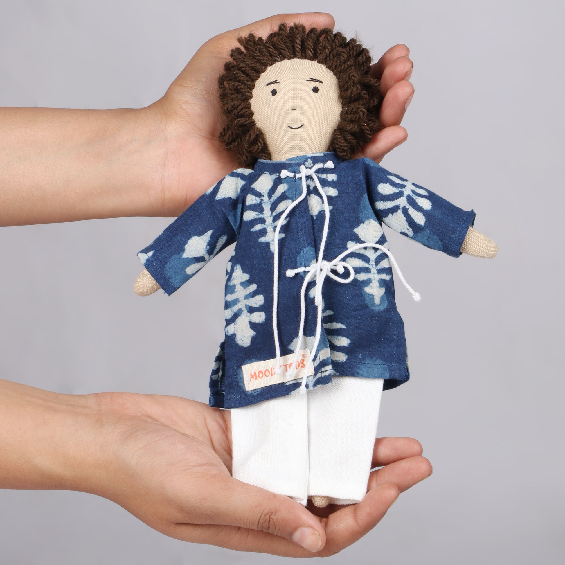 Holding 9 inch boy rag doll in hand with colorful outfit, made from child-safe, soft fabric