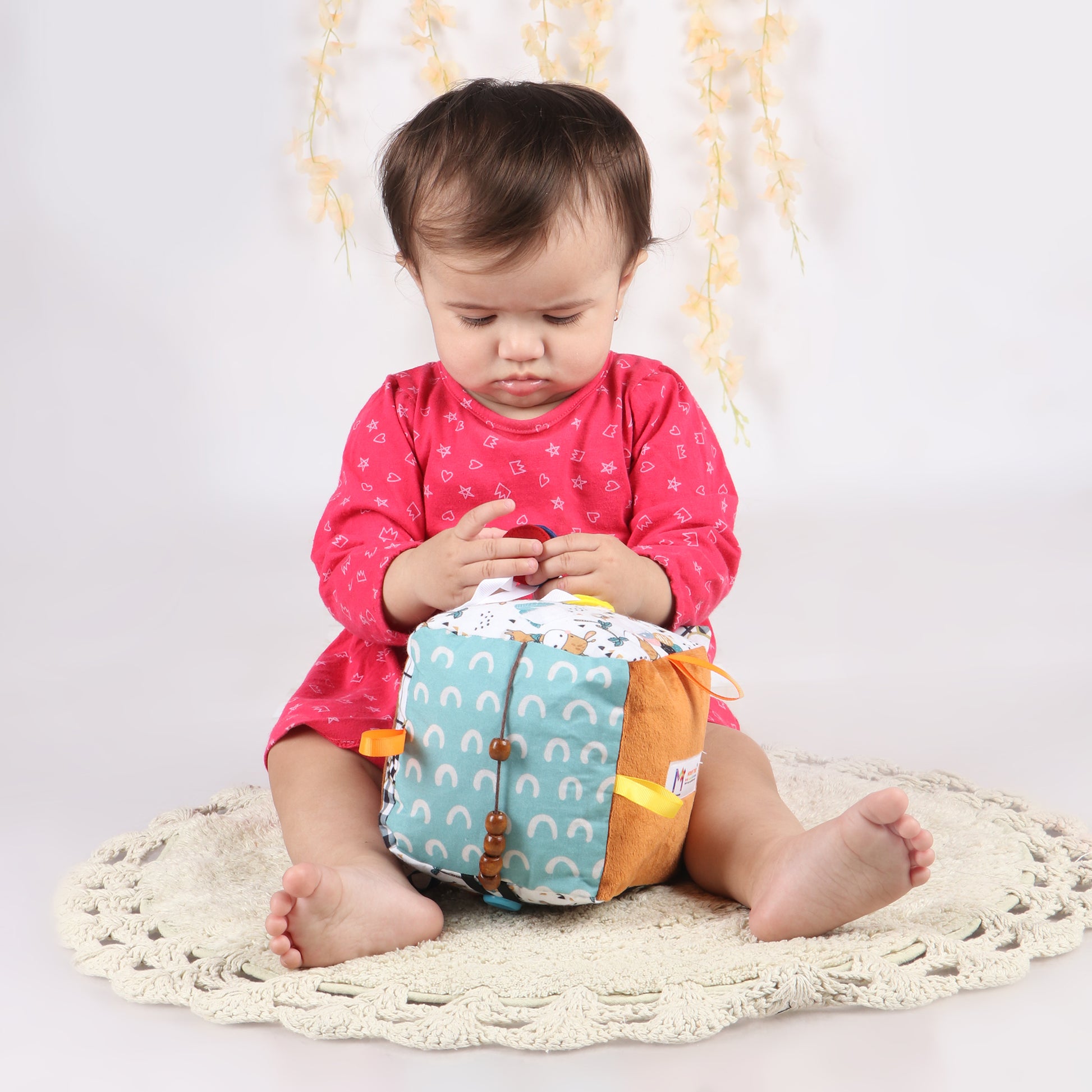 Toddler exploring soft fabric activity cube with interactive elements like ribbons, textures, and buttons for early childhood development