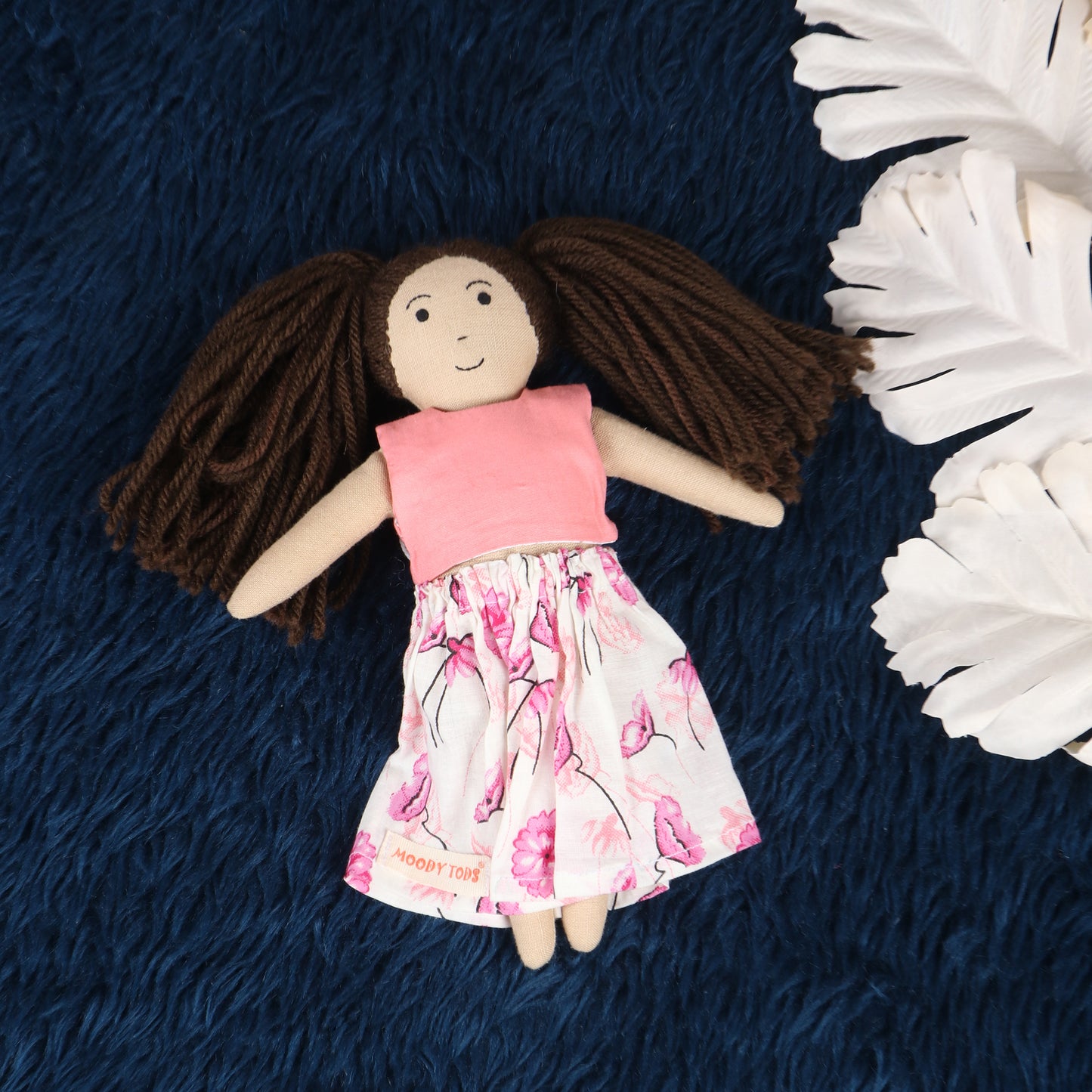 Front view of a 9 inch handmade fabric rag doll with embroidered facial features and a pink outfit with brown hair made of wool