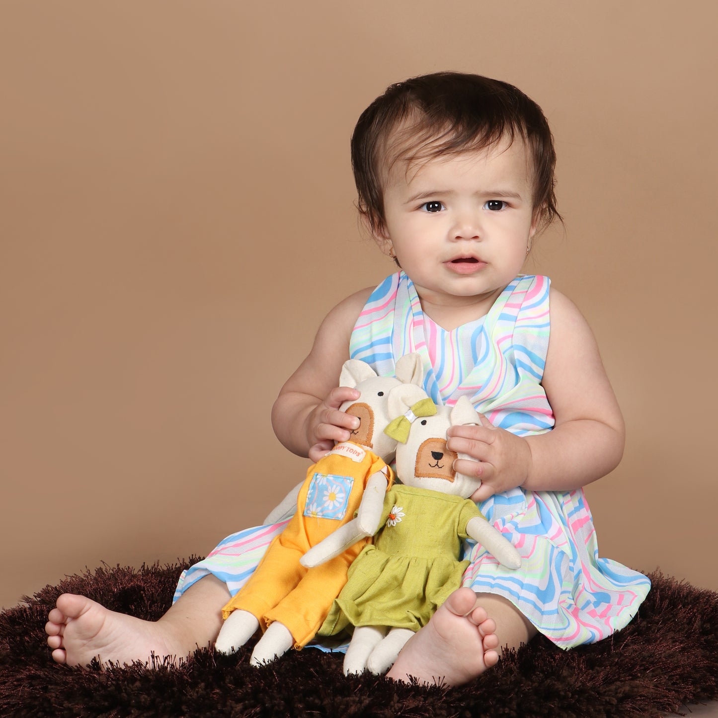 Toddler holding a pair of 12 inch soft fabric bear doll demonstrating its child-friendly size and wearing pastel green and orange colored outfit, ideal for toddlers and young children