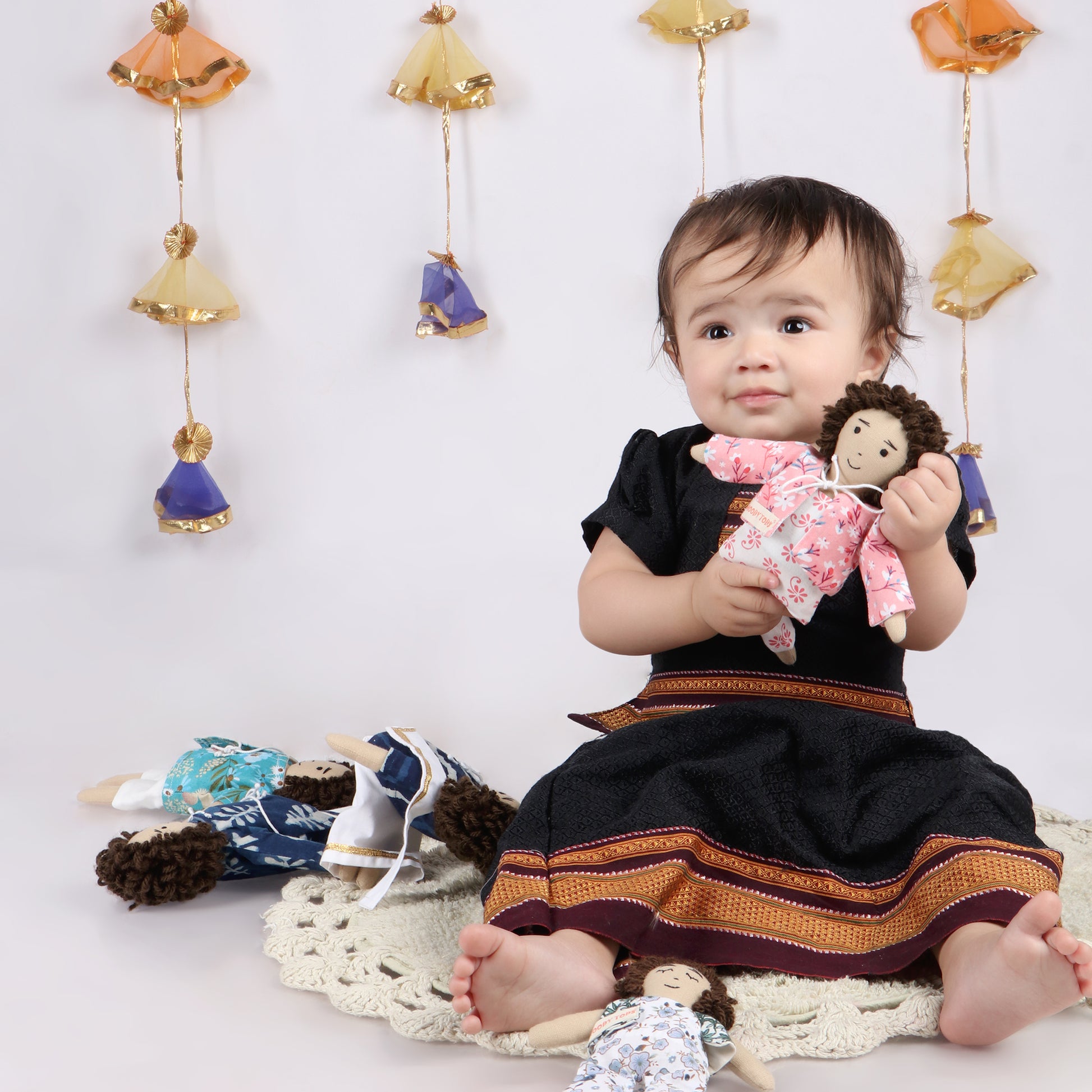Toddler holding 9 inch boy rag doll demonstrating its child-friendly size and comfort with other boy rag dolls scattered beside toddler